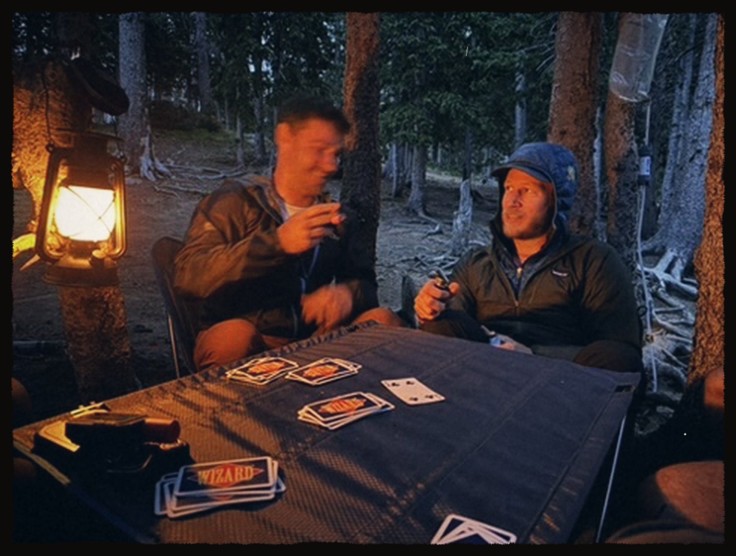 Two friends playing cards by lantern light at camp