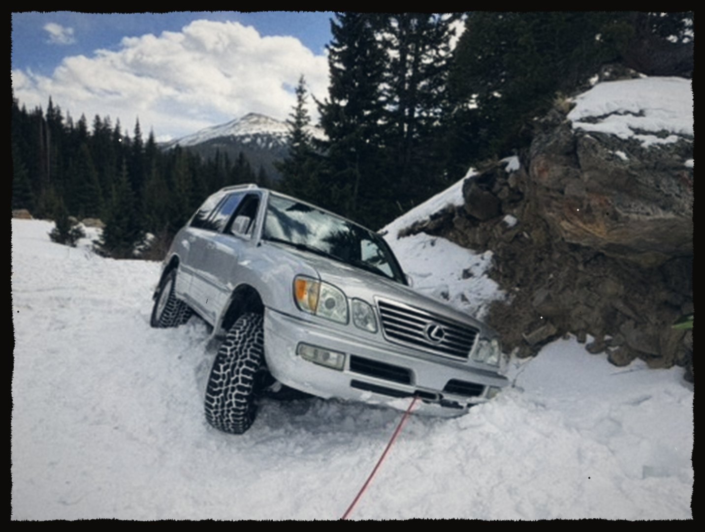 A silver SUV stuck in deep snow on a mountain road
