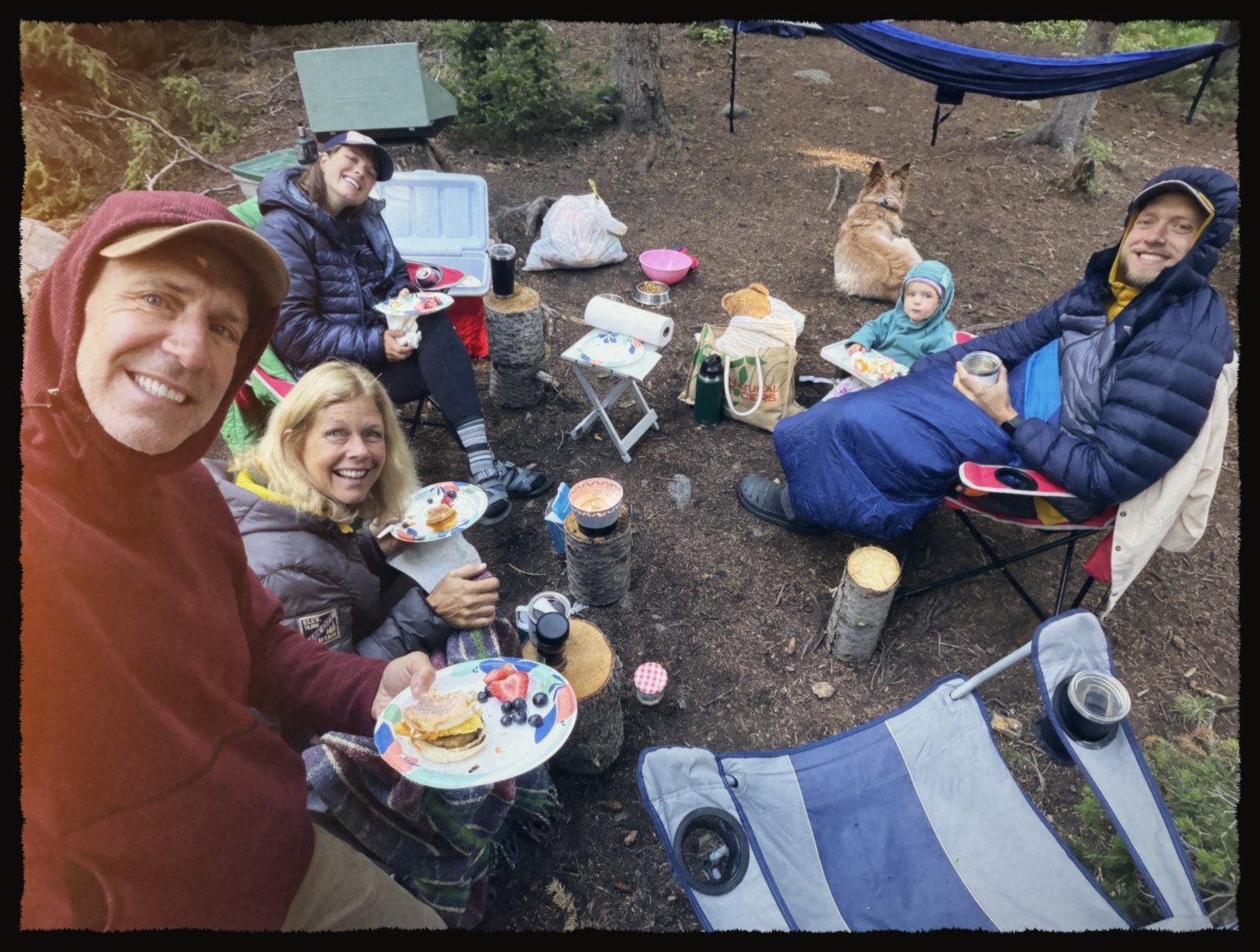 Group selfie at a campsite breakfast with a toddler and a dog